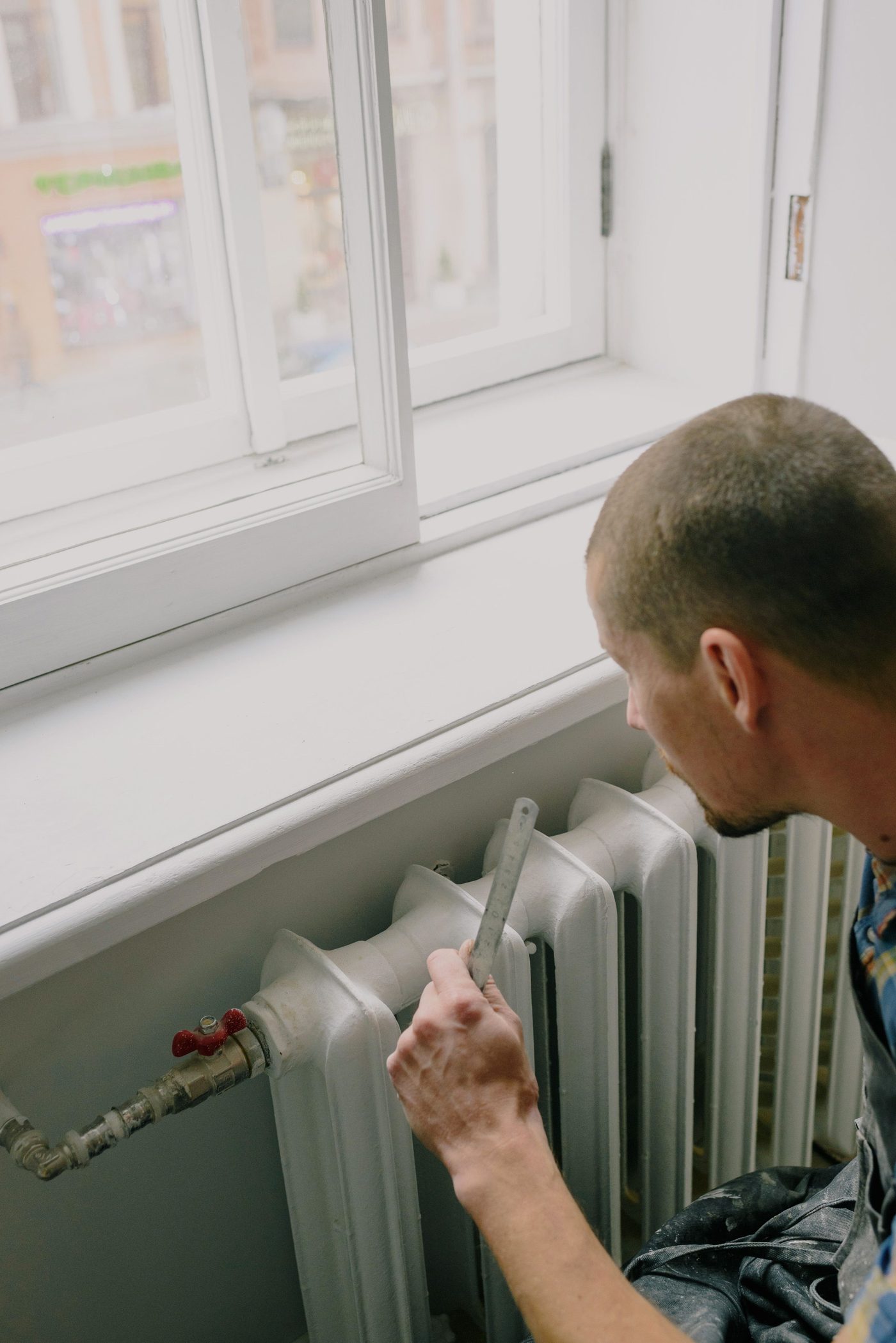 Workman measuring beside a cast iron radiator under a bright window