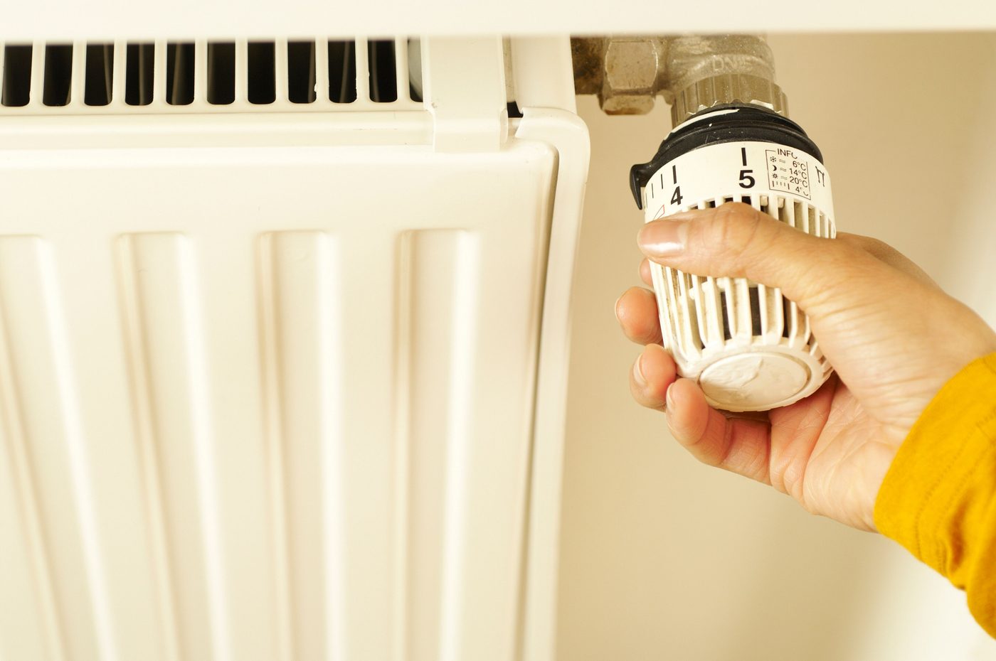 Hand turning a thermostatic radiator valve on a white radiator