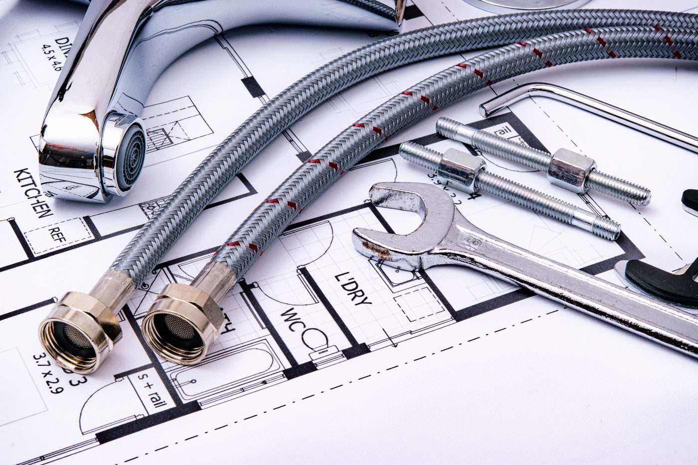 Braided tap hoses, a tap and spanners lying on a plumbing plan drawing