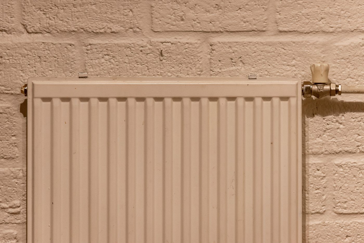 White panel radiator with a valve on a painted brick wall