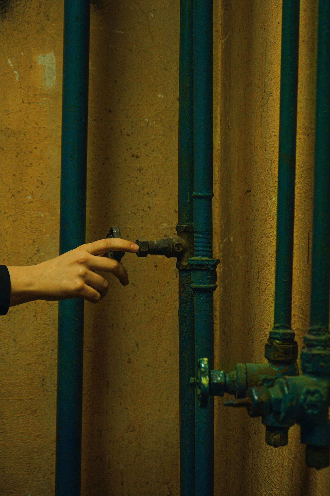 Gloved hand turning a valve on painted pipes in a dim cellar