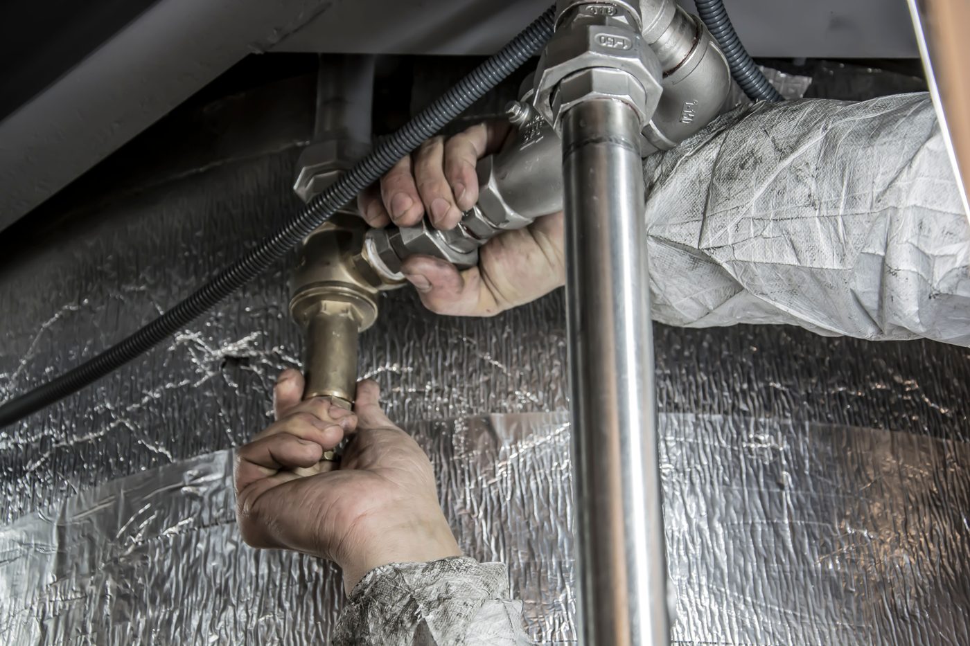 Plumber's hands working on a pipe joint beside foil insulation